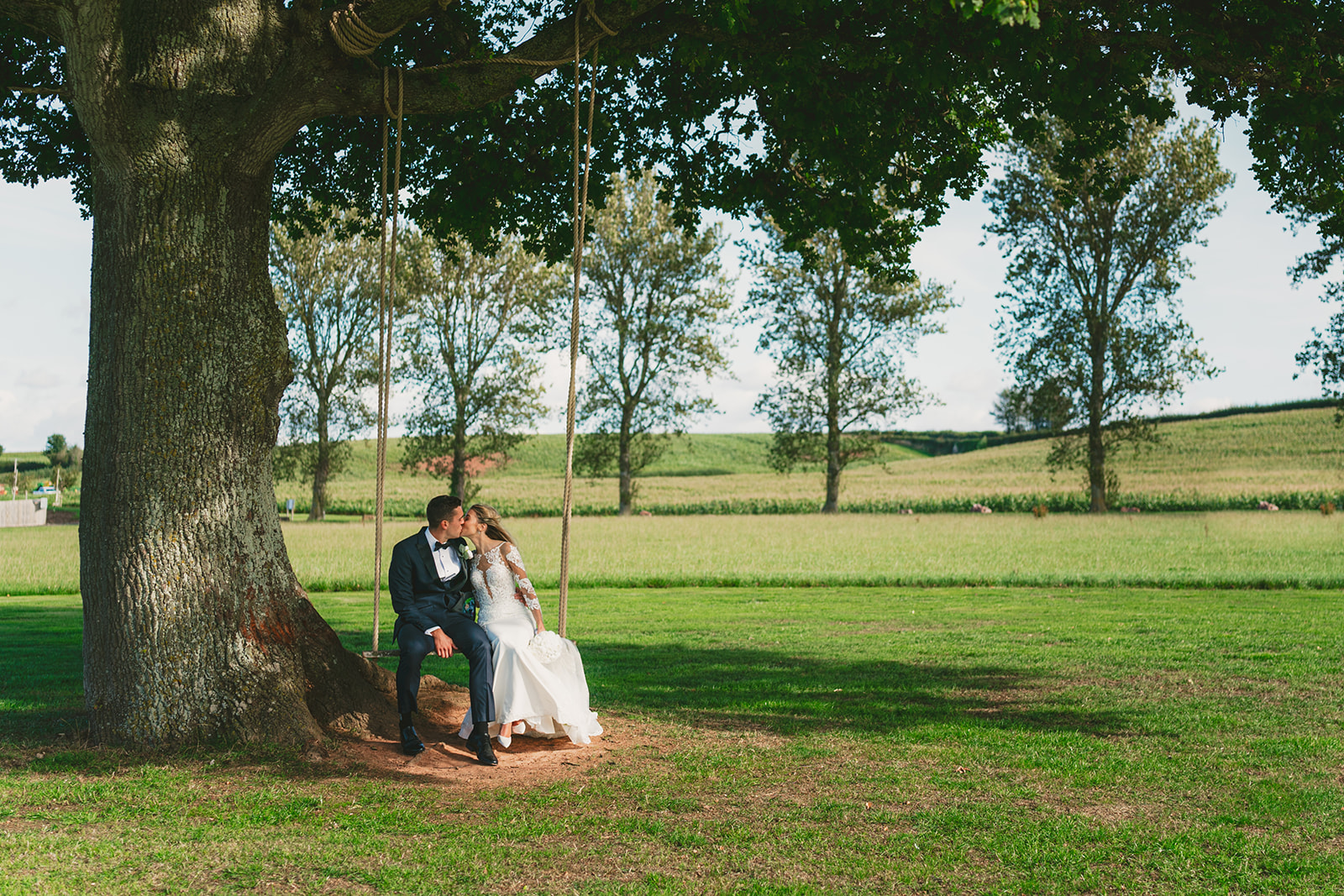 A bride and groom happily sitting on a swing in a serene field, captured beautifully by a Bristol wedding photographer.