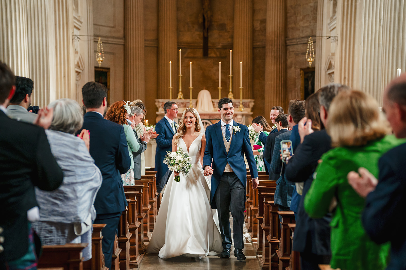 A bride and groom walking down the aisle of Prior Park Church in Bath during their wedding ceremony.