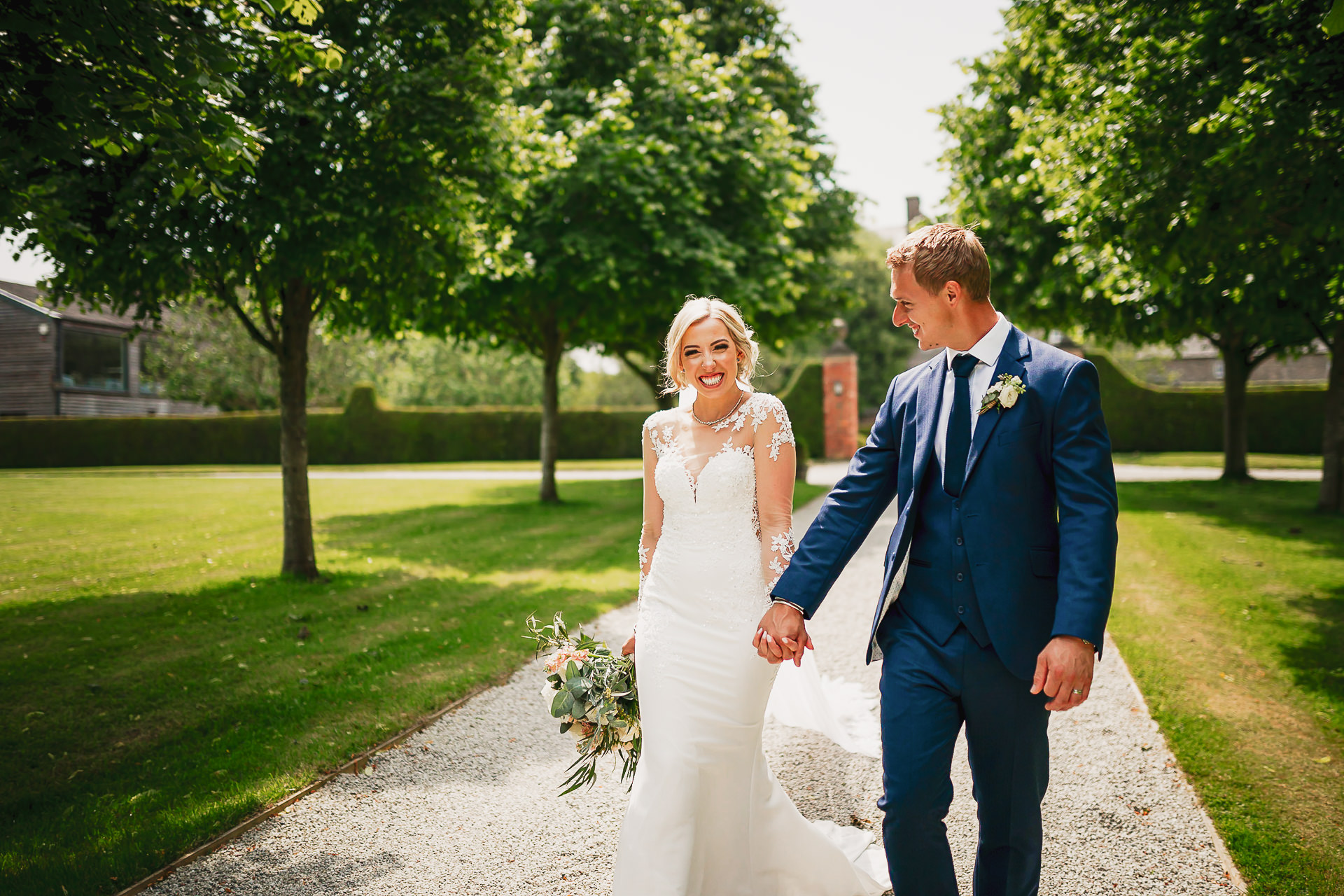 A bride and groom walk, hand-in-hand through the grounds of Kingston estate in Devon