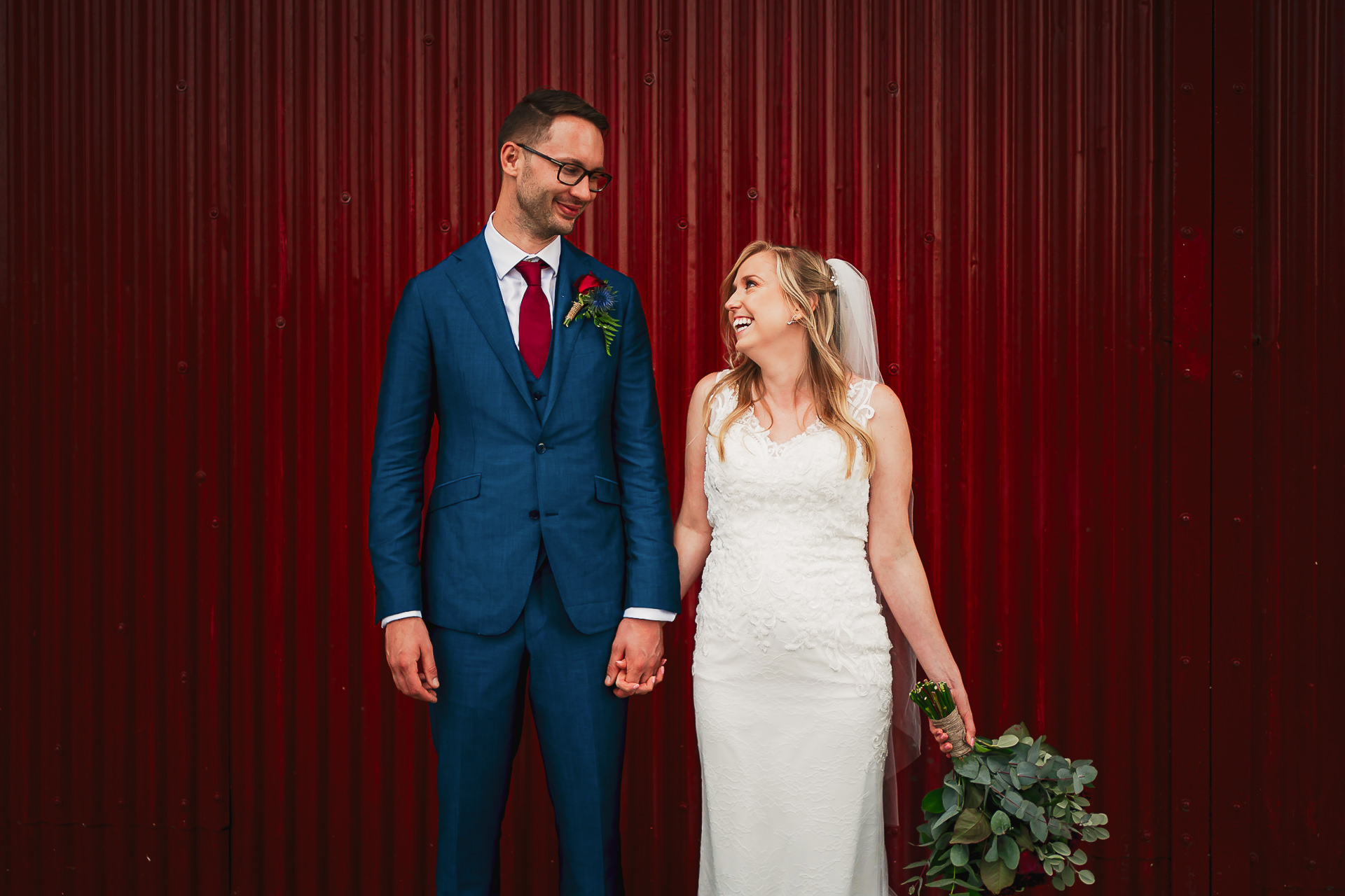A bride and groom stood next to a red door at the Waterside in Bristol