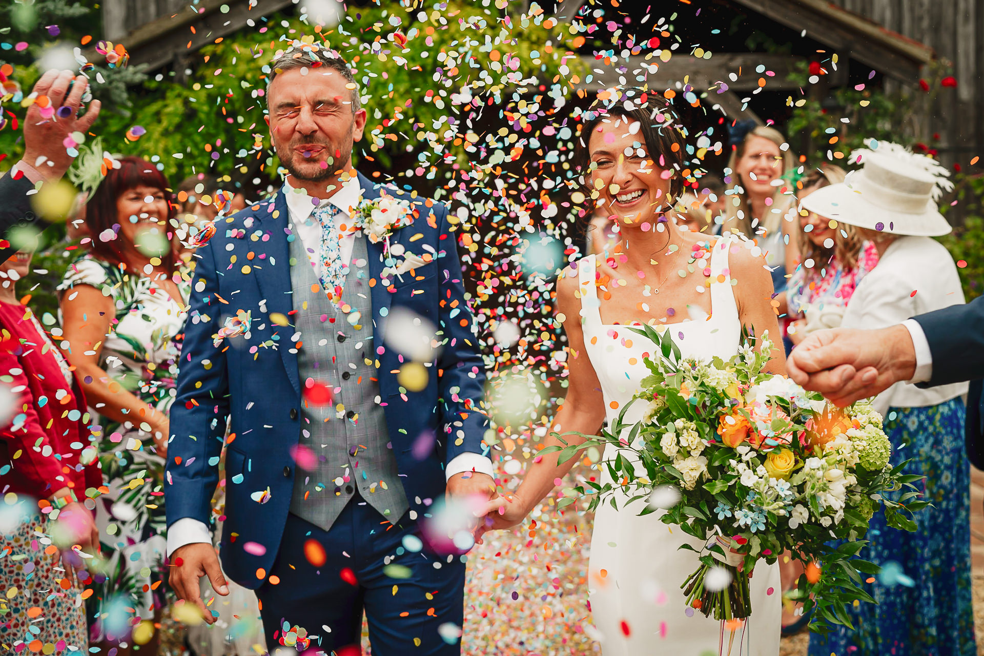 A bride and groom getting covered in very colourful confetti at the yArlington barn in Somerset