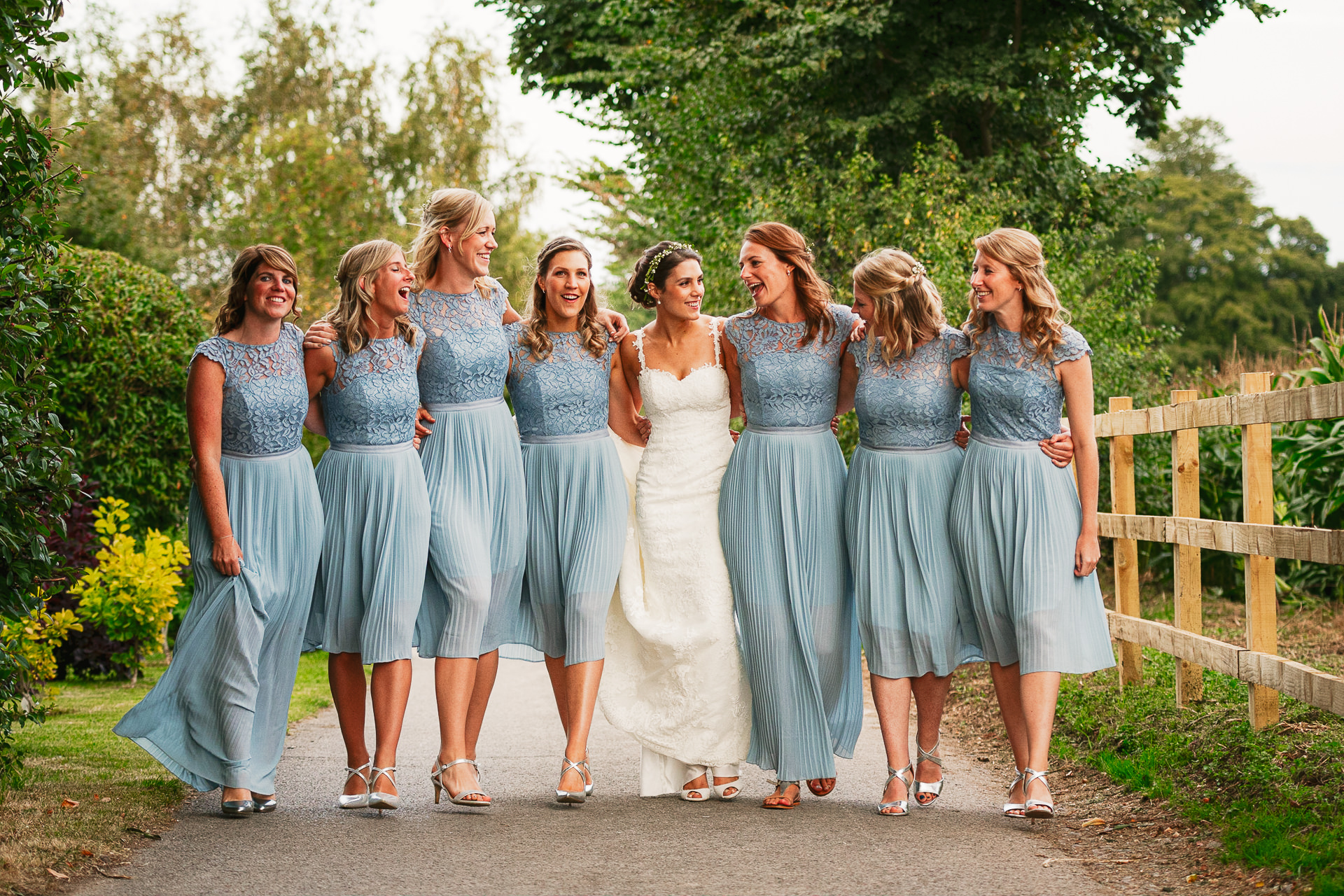 Bridesmaids in blue dresses, walking arm in arm with Bride in the country in Wiltshire