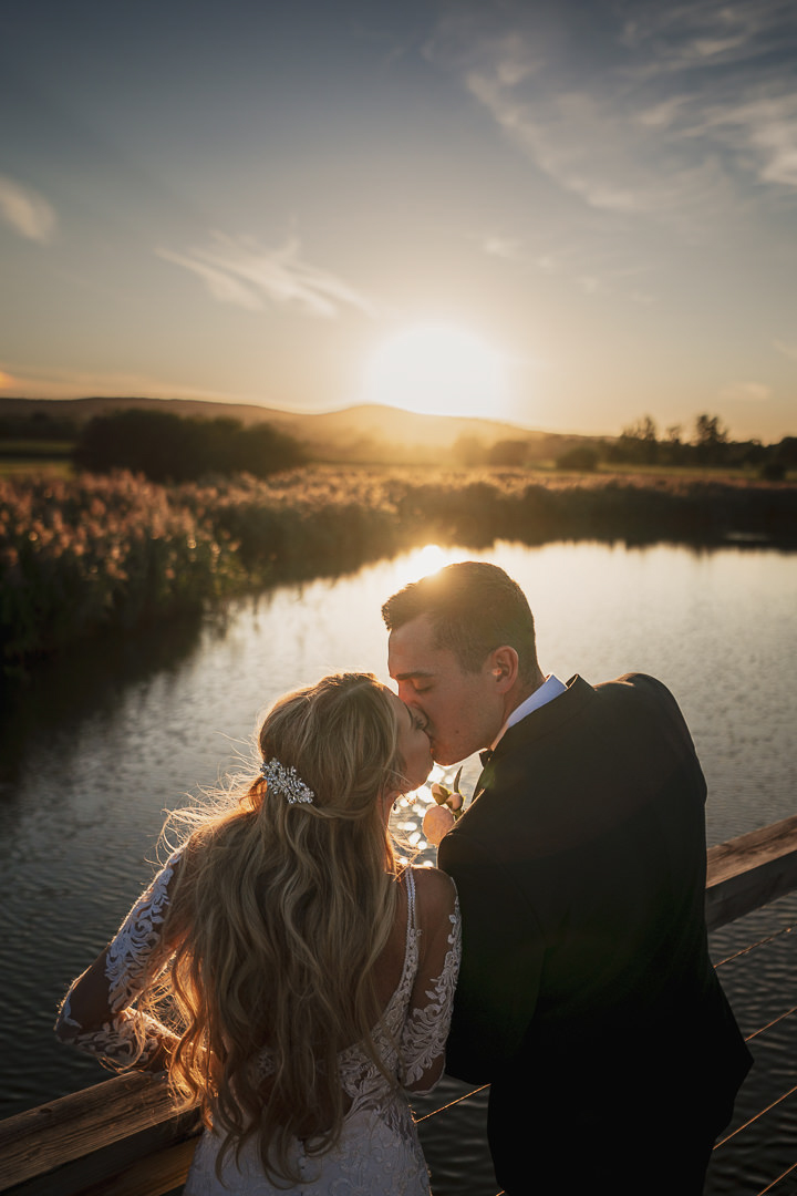 A bride and groom kiss in the sunset on the pontoon at quantock lakes, Somerset