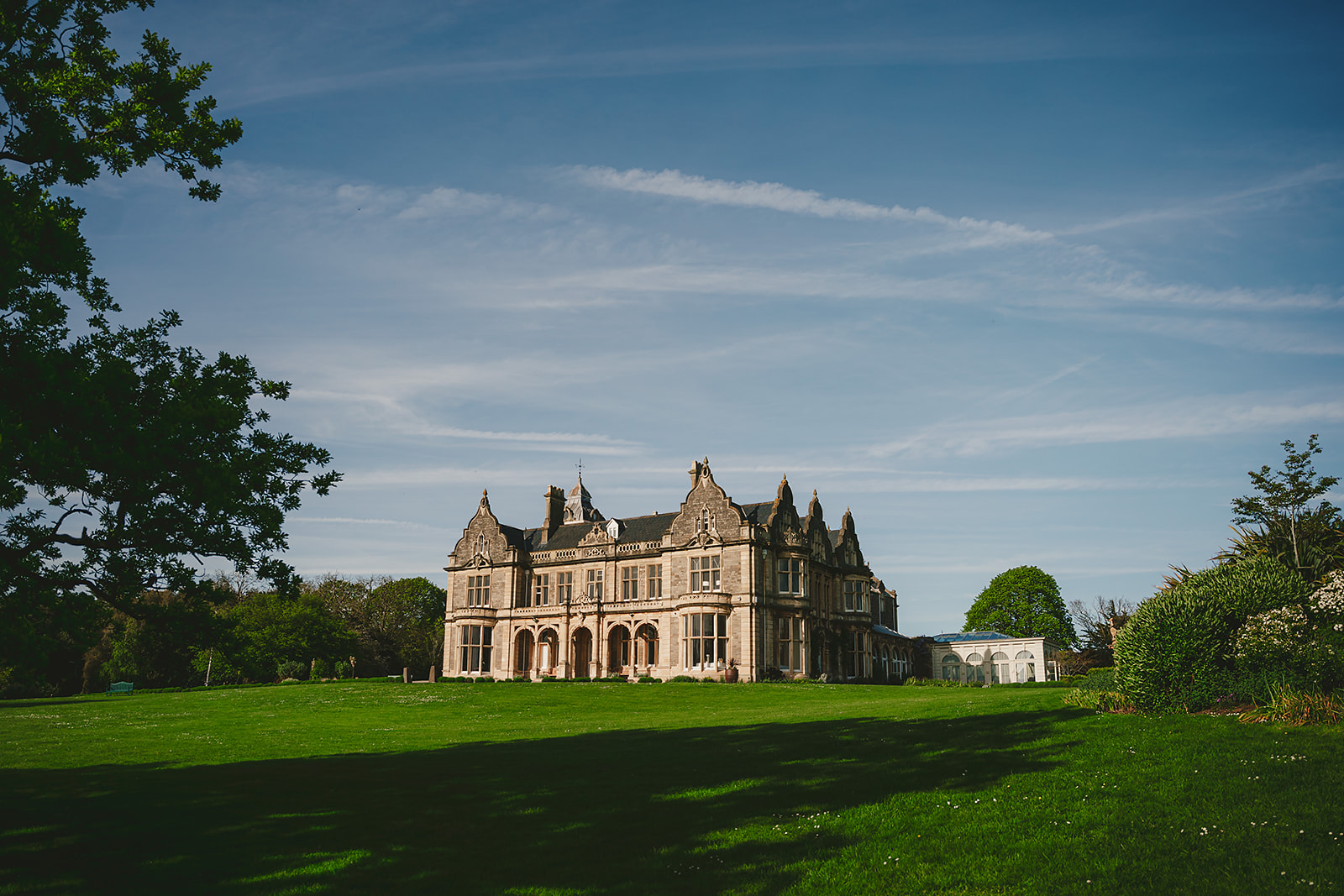 A grand mansion nestled in the center of a lush grassy field, perfect for captivating wedding photography at Clevedon Hall.