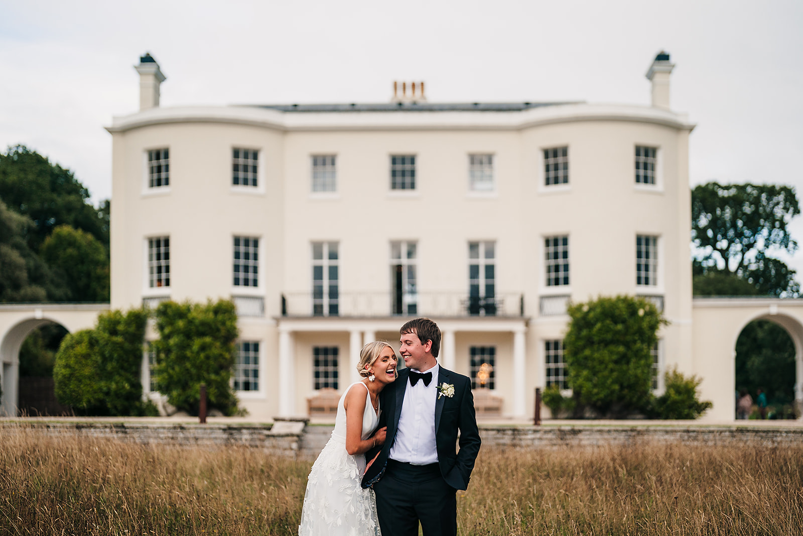 A Devon wedding photographer captures a bride and groom in front of Rockbeare Manor, a large white mansion.