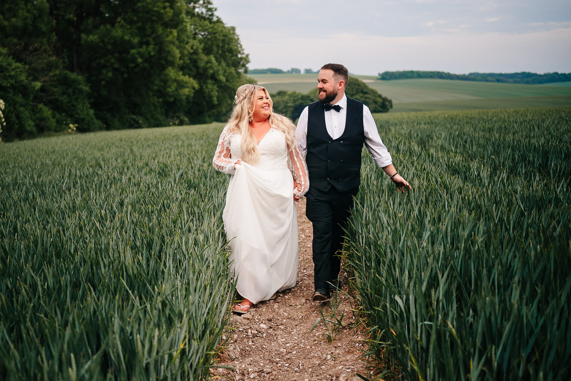 A bride and groom strolling hand in hand through a picturesque field of wheat, capturing the essence of natural beauty at The Gathering, a barn wedding venue.